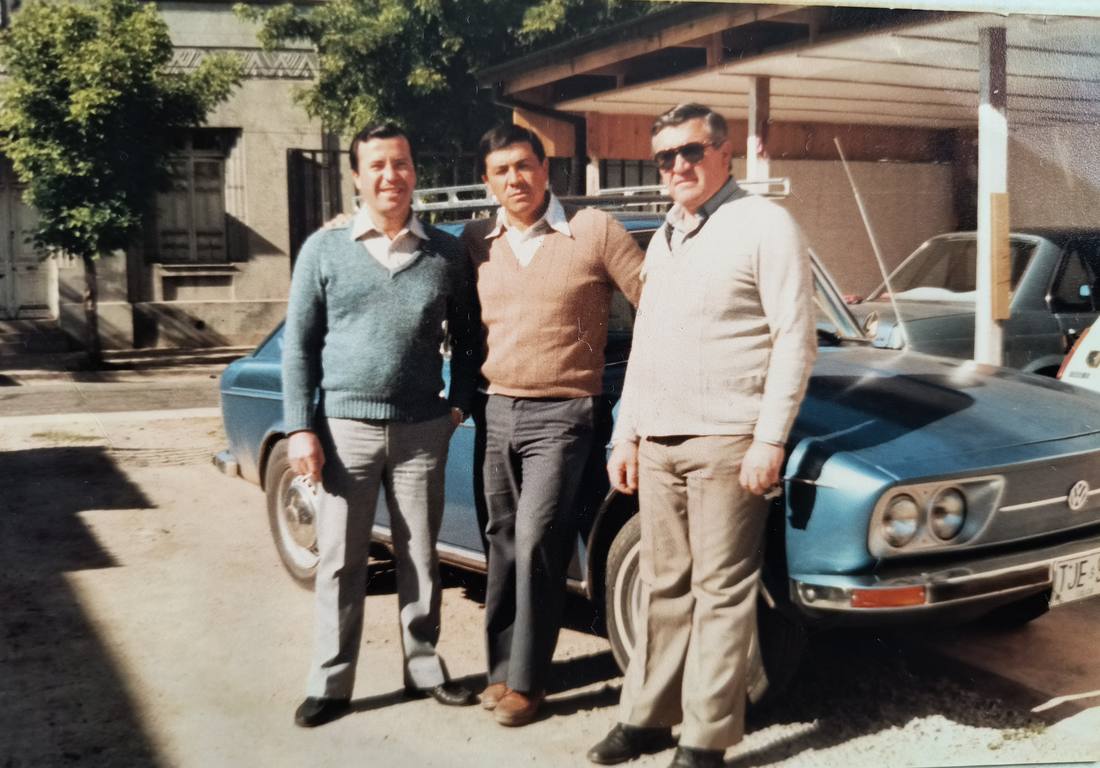 Fotografía de los primeros años del negocio: tres hombres posan junto a un automóvil azul en el patio del local.